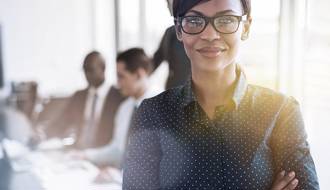 Smiling female professional with obscured male professionals at their desks in background